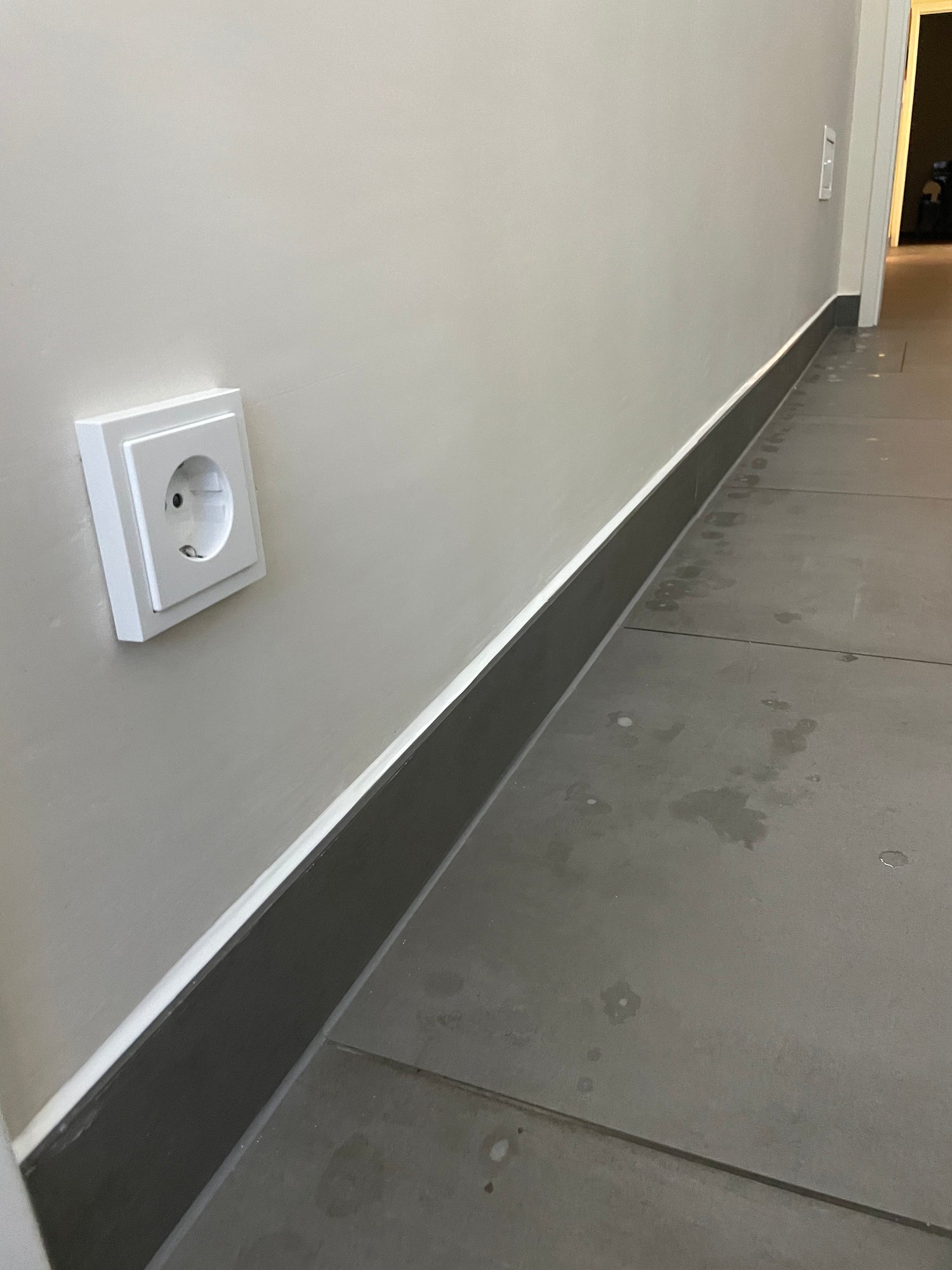 Eine neu versiegelte Sockelleiste mit weißen Silikonfugen oben drauf und grauen Silikonfugen zum Bodenanschluss.