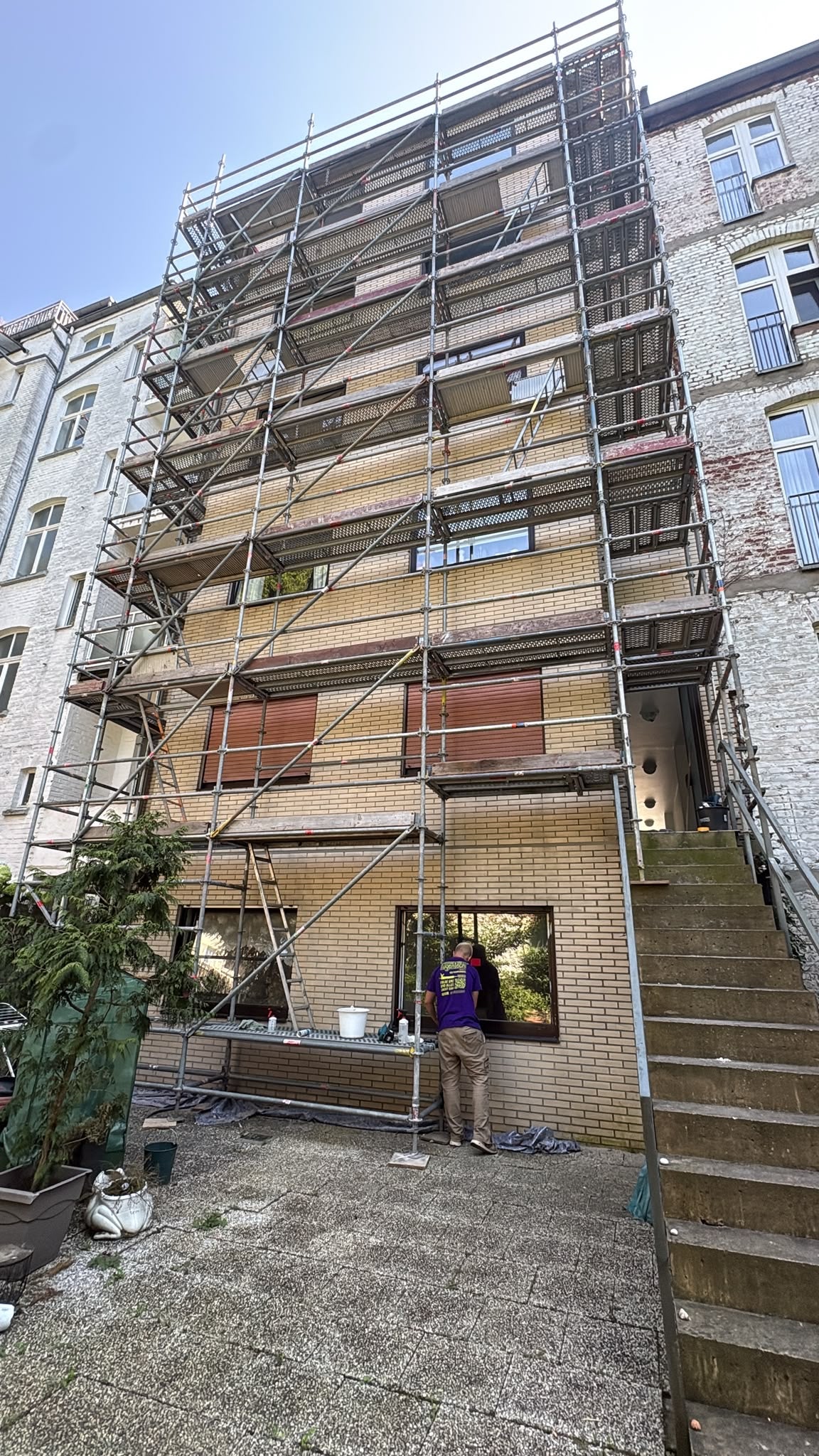Gerüst an einer Riemchenfassade. Ein Mitarbeiter steht an der Fassade und schneidet alte Fensterfugen heraus. Das Gebäude ist 7 Stöckig und in Düsseldorf